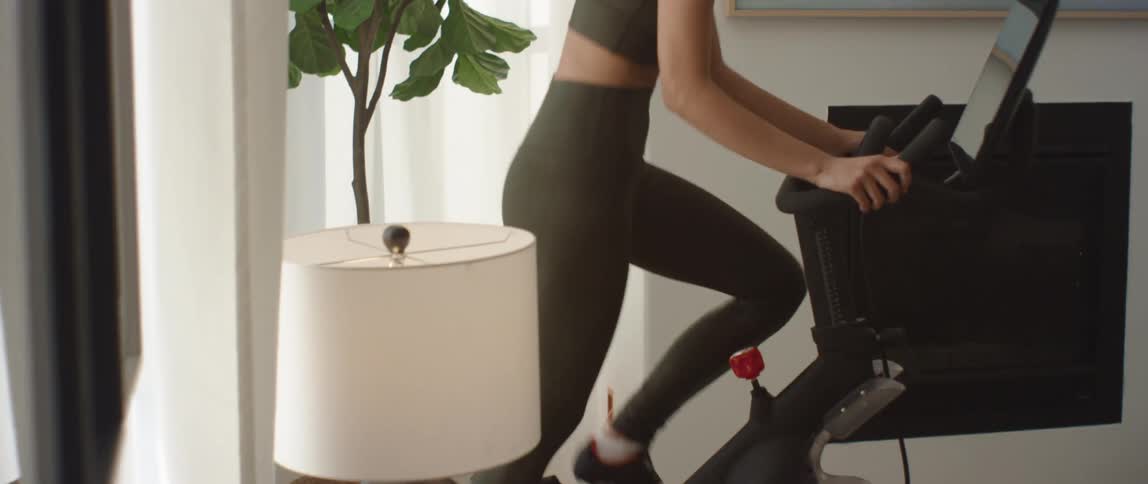 Young fit woman in green sports clothing exercises on a static cycle in the living room at home