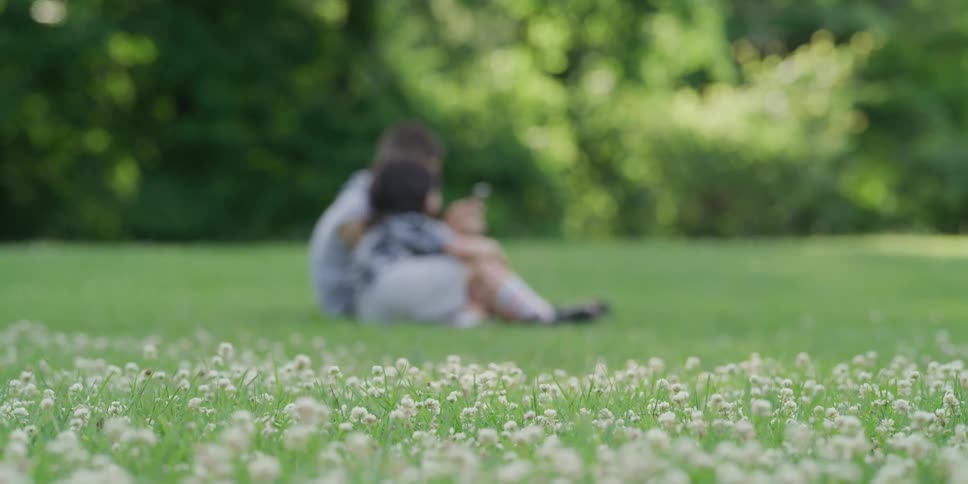 Two boys sit in an open grass area playing a hand held video game