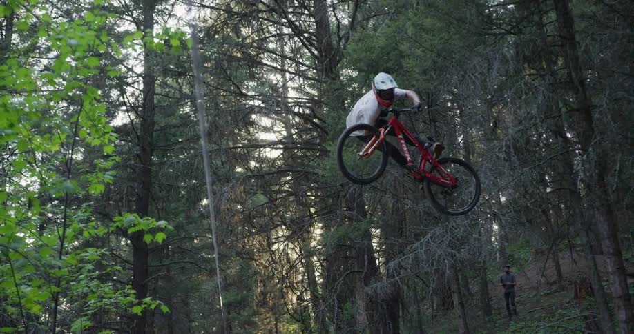 Man on a red bike doing tricks and jumps over slopes on a dirt path in a forest