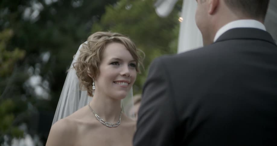A bride smiles and blushes while standing in front of her groom