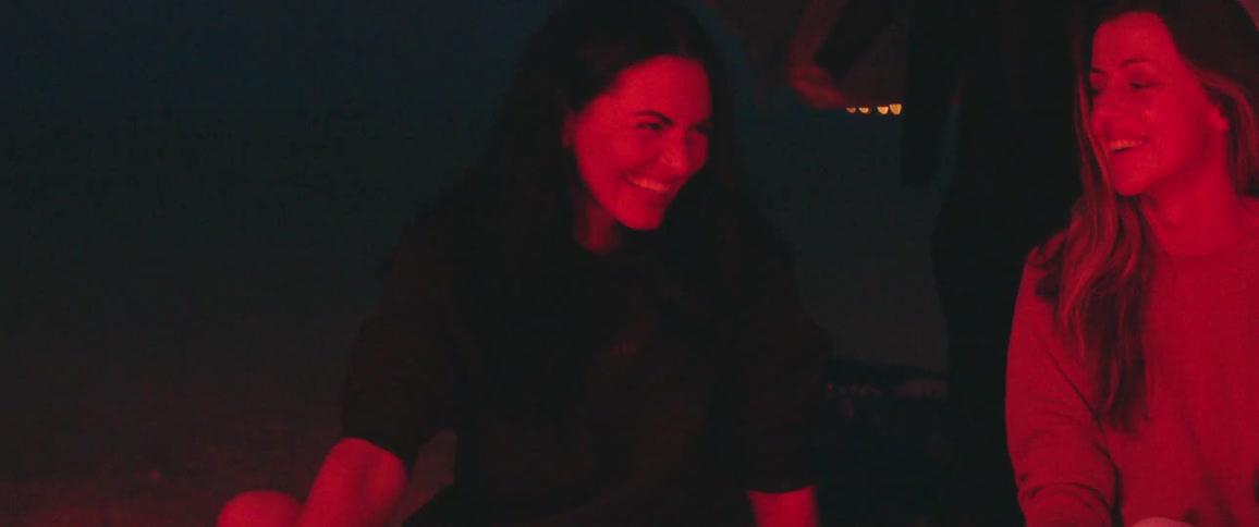 Group of friends under a red light sitting outdoors at night talking and laughing