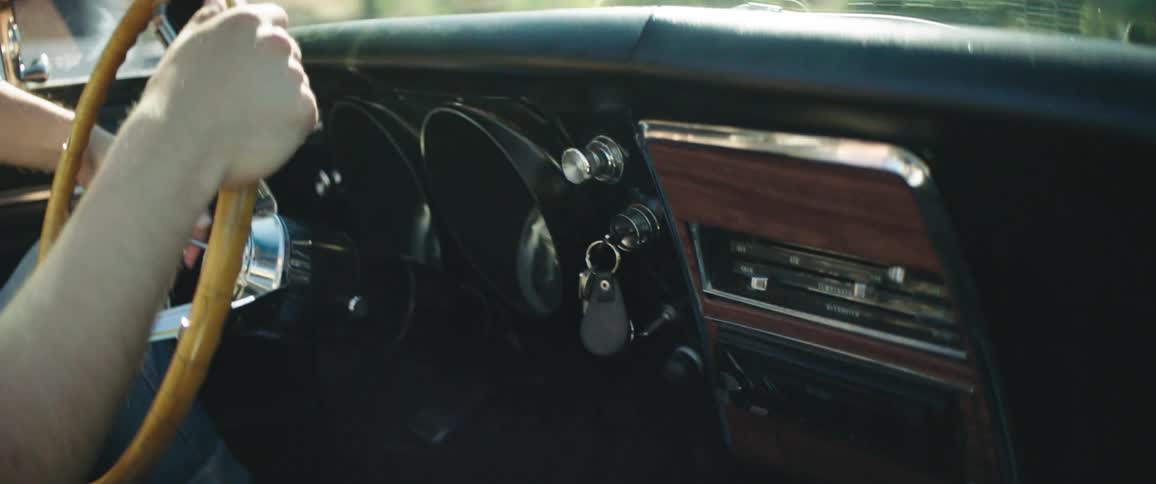 Man driving in an antique car reaches over to turn on the radio