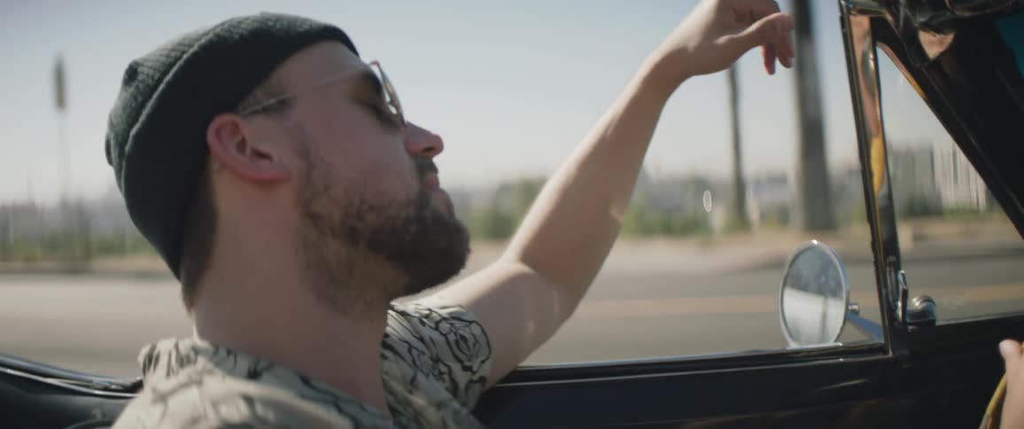 A man driving a vintage car with the top down on a city street