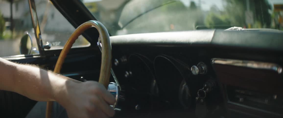 A man drives a vintage convertible with the roof down through a neighborhood
