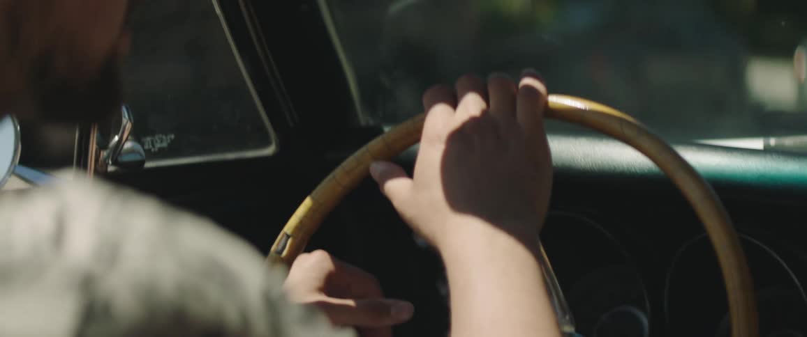Man driving a vintage car points with his finger at something right of the road