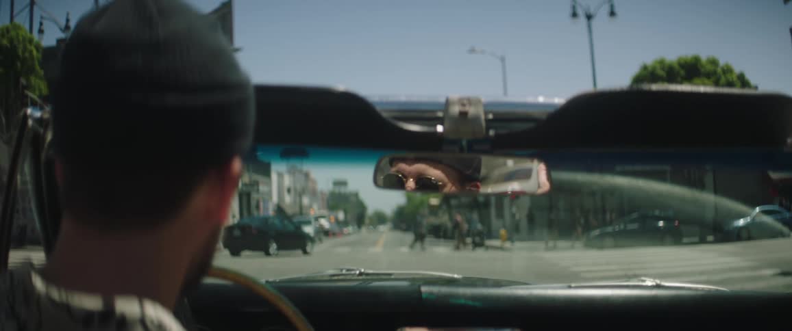 Man and a woman in a vintage vehicle stopping at a red light down a street in downtown la