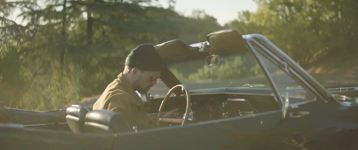Man starts and drives away in a convertible car on a rural road in the forest at sunset