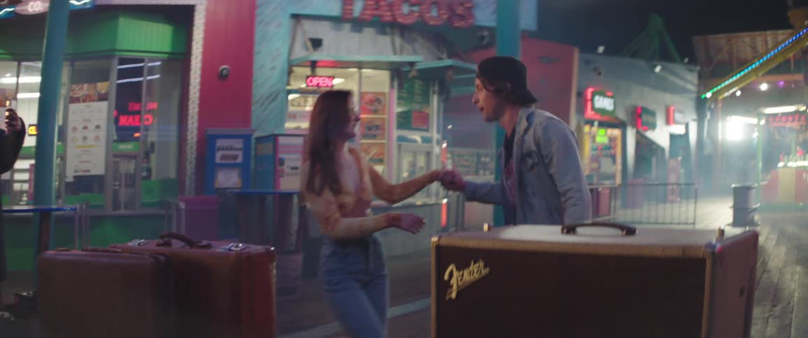Couple dances at night near suitcases with storefronts in background