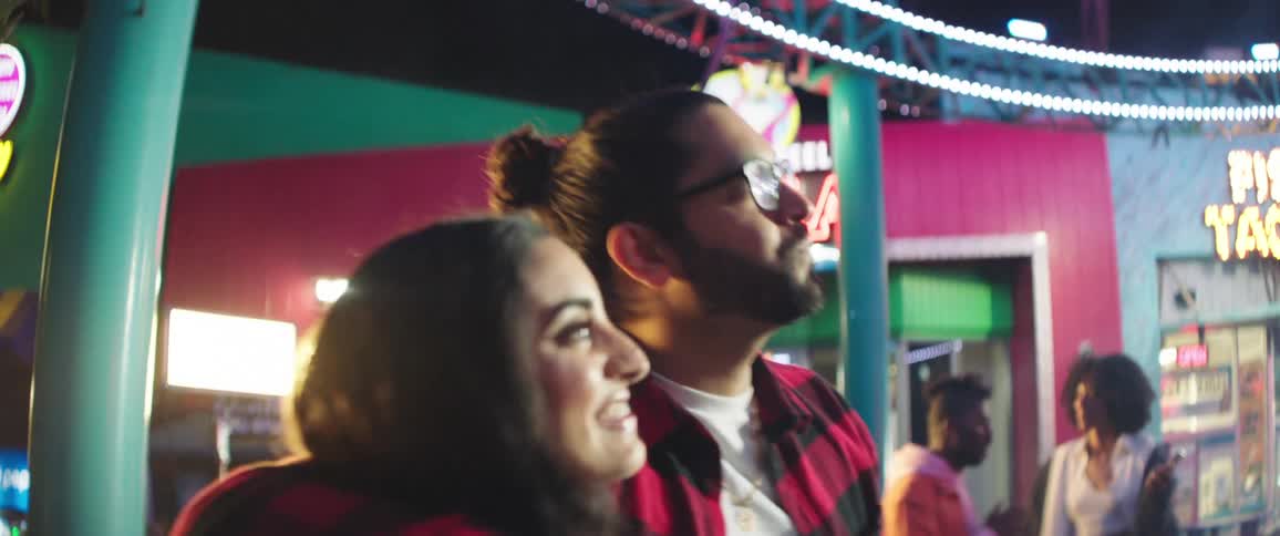 Young couple dancing and hugging in the food court of an amusement park at night