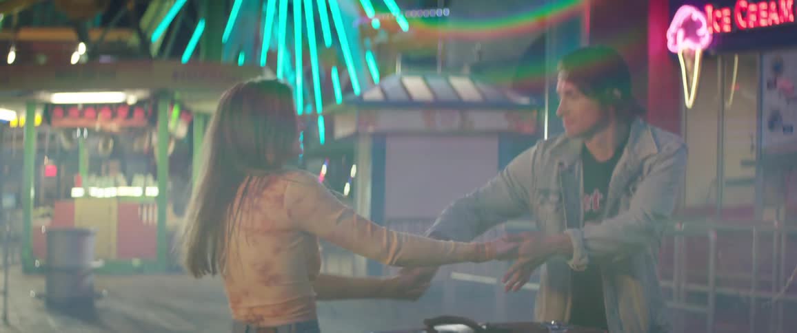 A young man and woman dance together on a carnival ground at night