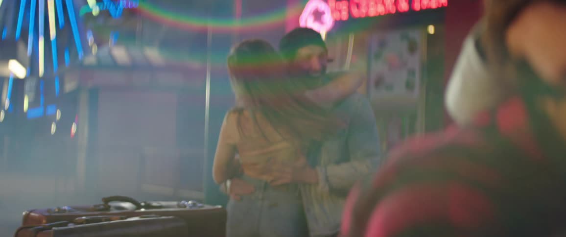 Young couple happily dancing on a colorful amusement park at night