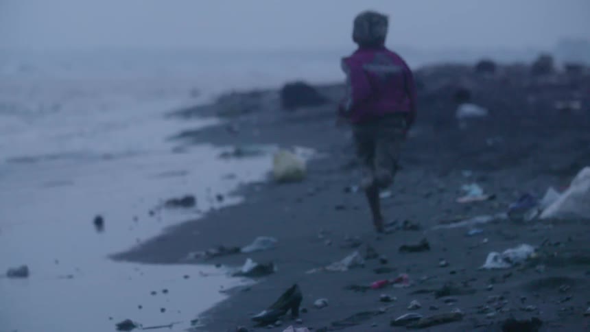 A man is running along some debris by the shore