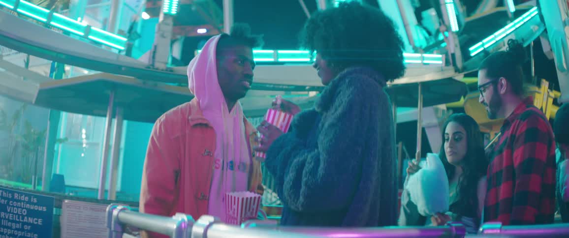 Friends laugh and eat junk food while waiting in line for a ferris wheel