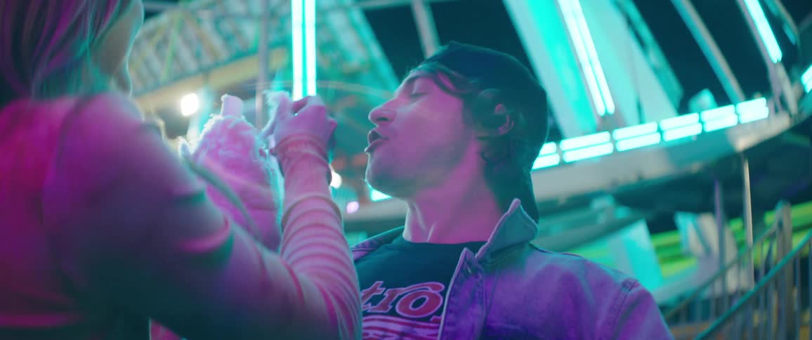Young couple eating cotton candy next to a ferris wheel at night