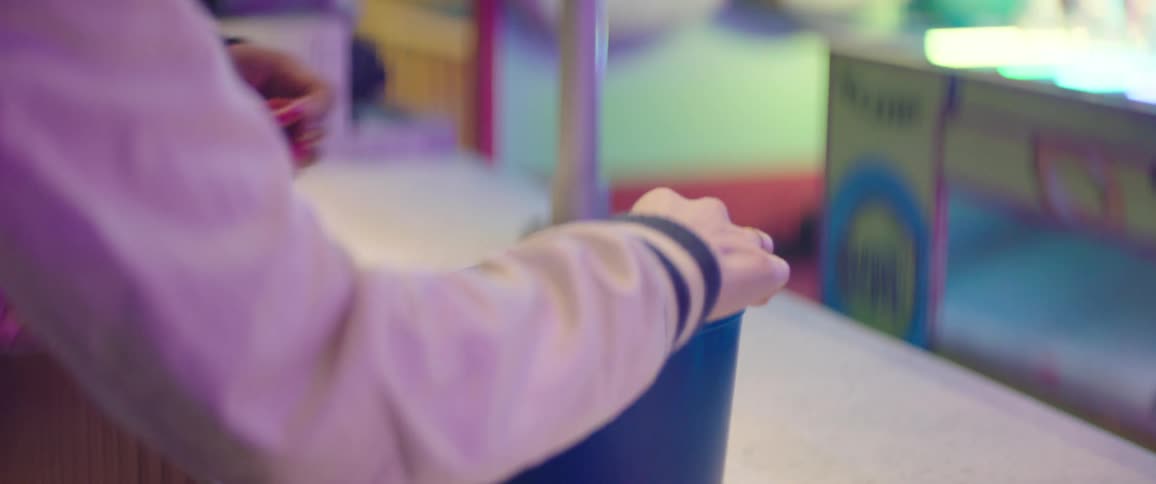 A couple picking up red plastic rings from a blue bucket in a stall on an amusement park