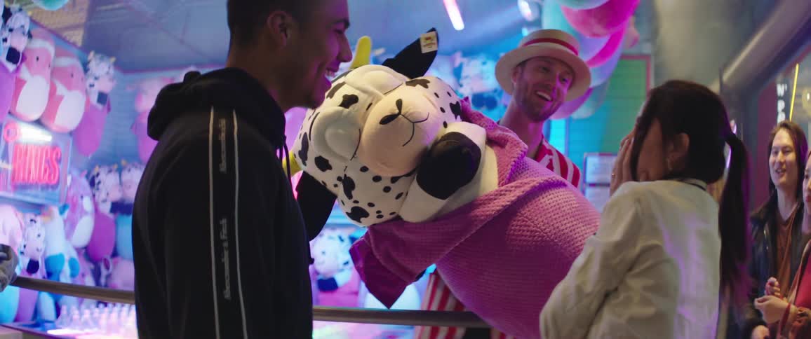 Carnival worker hands a large stuffed animal over to a woman with her boyfriend for winning a game