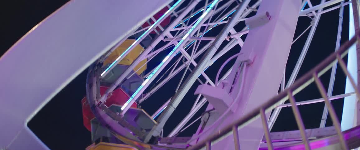 A ferris wheel with lights with the sky in the background and a fence in the foreground
