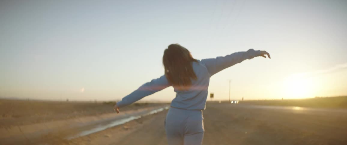 Young woman in sports clothes walking on a rural field at sunset