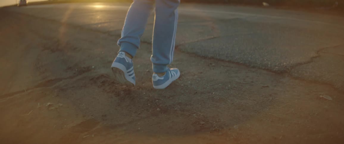 A person with sweatpants and sneakers walking on the road with the sky and clouds in the background