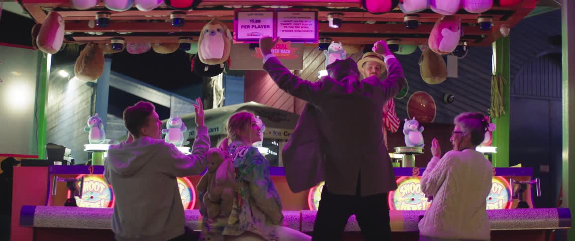 An elderly man jumps up from his stool and cheers after winning a carnival game