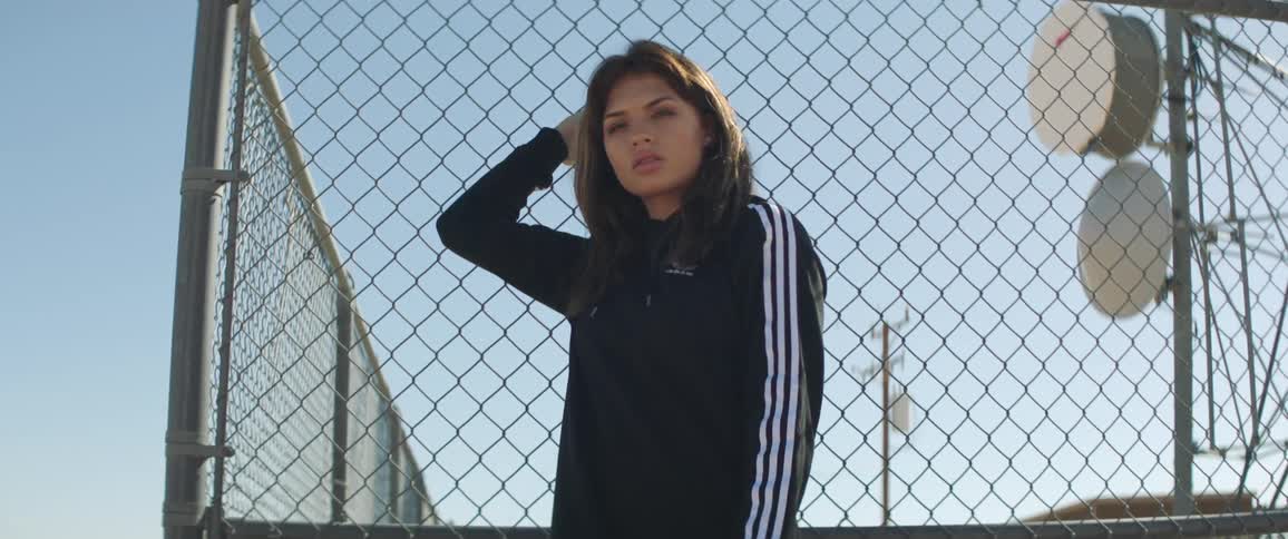 A woman standing next to a fence with an antenna an utility pole the sky and clouds in the background