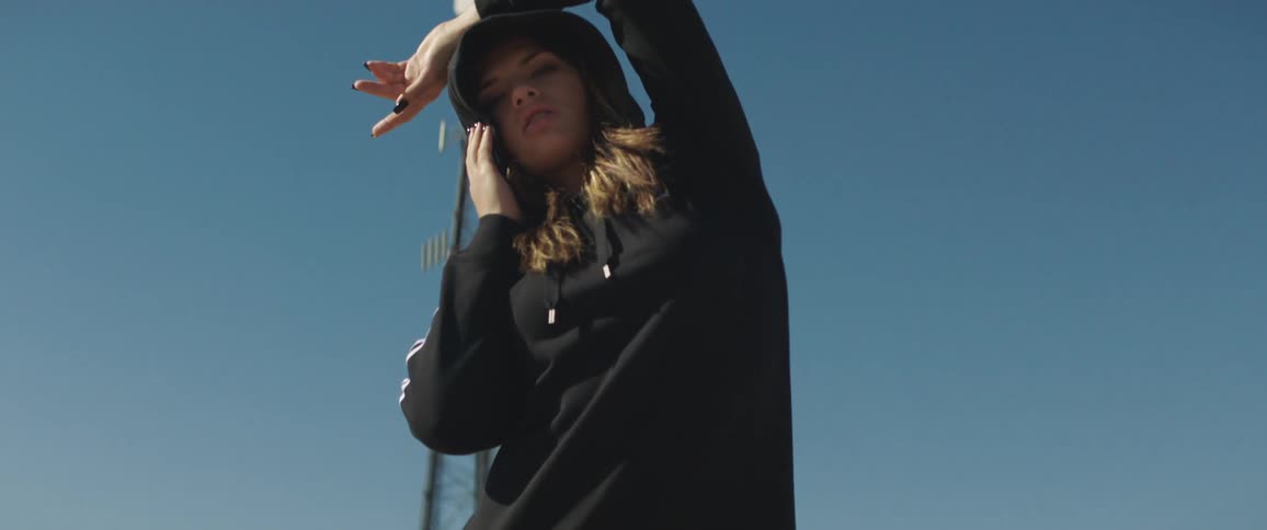 Woman wearing a black hoodie posing at the camera in front of a signal tower