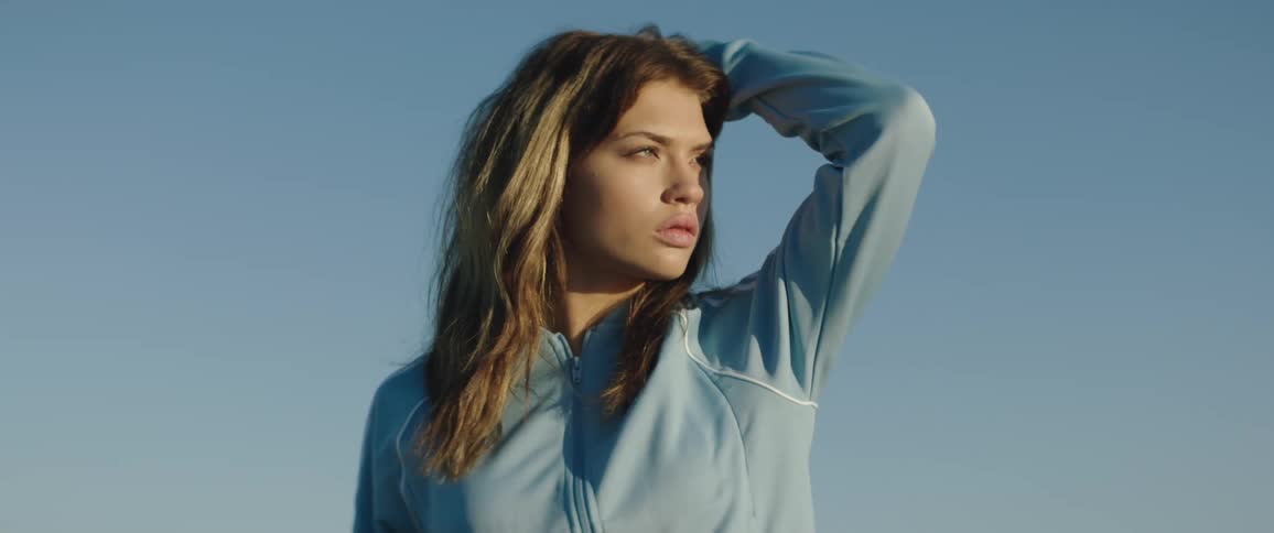 Young woman wearing sports clothes models looking at the horizon outdoors at evening