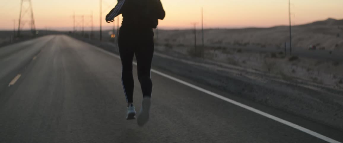 Silhouette of a woman on sports clothes jogging on an empty road at sunset