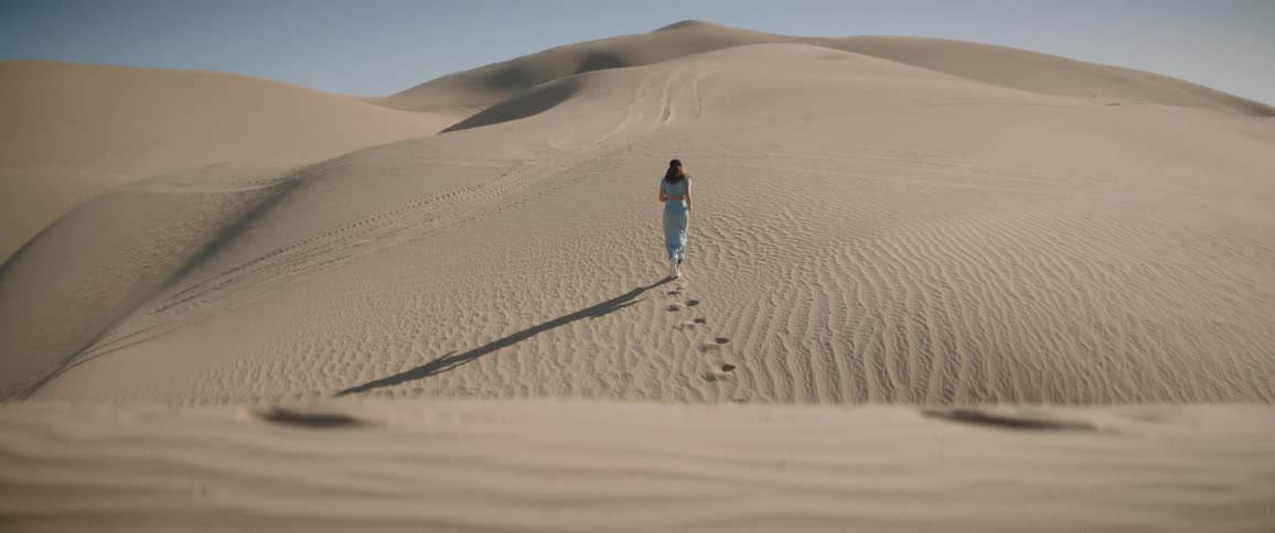 A woman with sneakers running in a desert with sand with the sky and clouds in the background