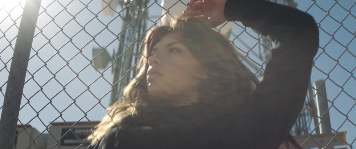 Woman reclined on the wired fence of a transmission tower looks at the camera