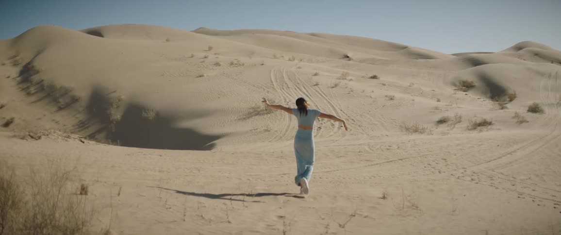 A woman stretches her arms out and over her head as she walks in the desert