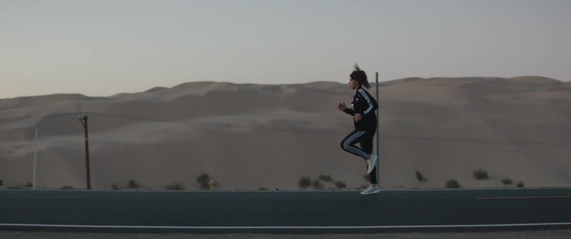 A woman running in place then jogging with utility poles a sand dune the sky and clouds in the background