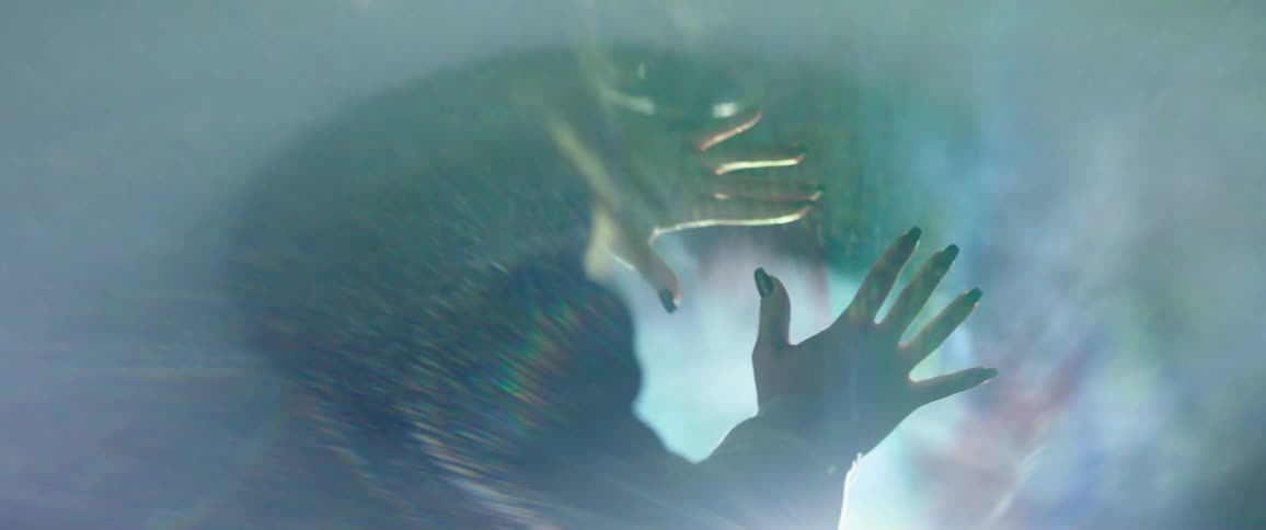 Woman stands with hands outstretched toward a projector creating a rainbow of color while her hair blows in the wind