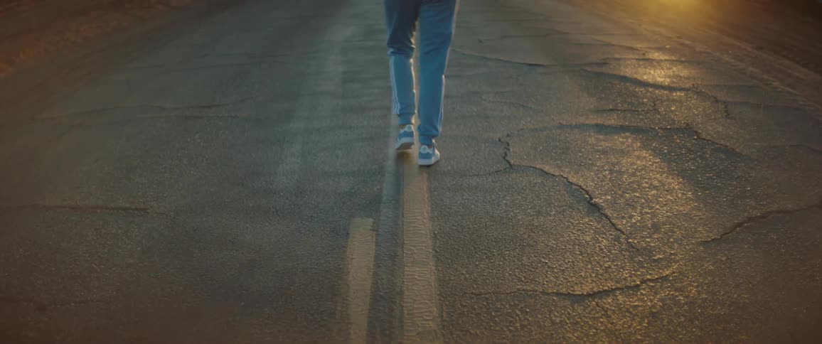 A woman walks down the middle of a road in the countryside wearing a matching sweatsuit