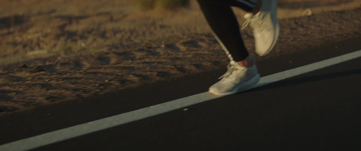 Woman in sports clothing running on a road in a rural area at sunset