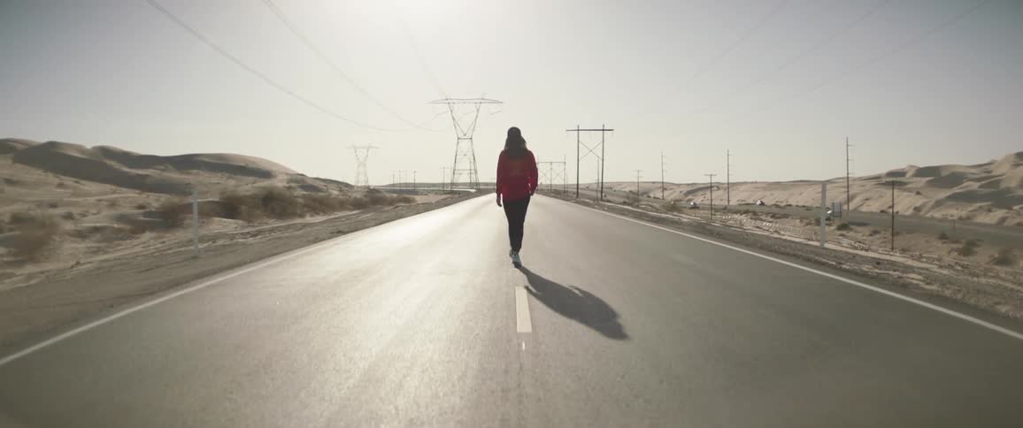 Young woman walking on an empty road through the desert at day time