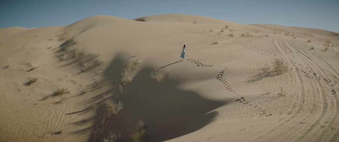 Woman in a blue dress walking over a sand dune in the desert