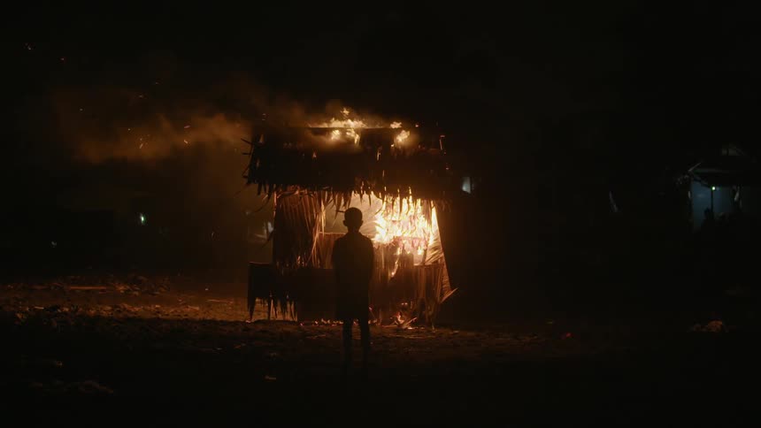 A person is watching a hut burn at night