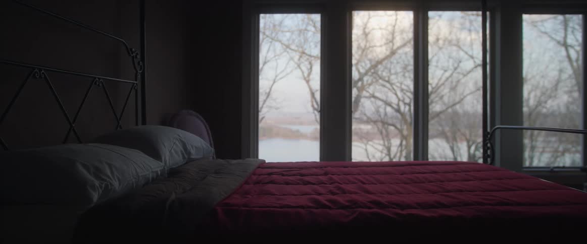 Red bed sheets over a bed in a dimly lit bedroom with a view to a winter landscape
