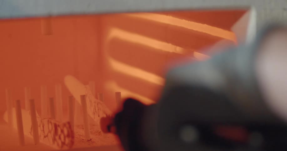 A person wearing gloves uses a tong to take knives out of a red hot blacksmith electrice furnace