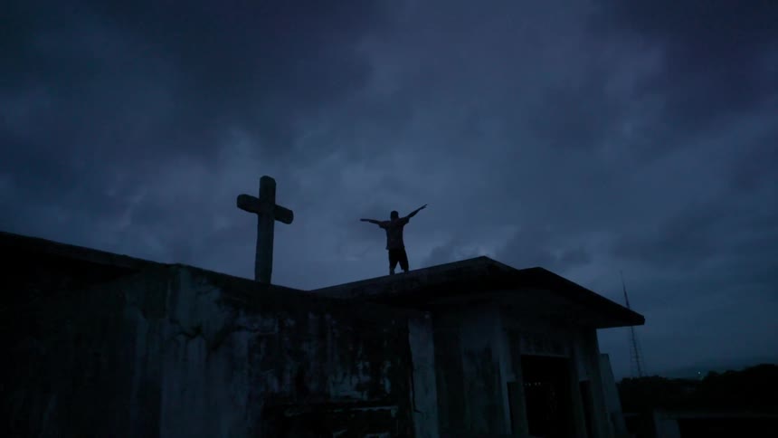 A person standing on top of a house stretches his arms out at night
