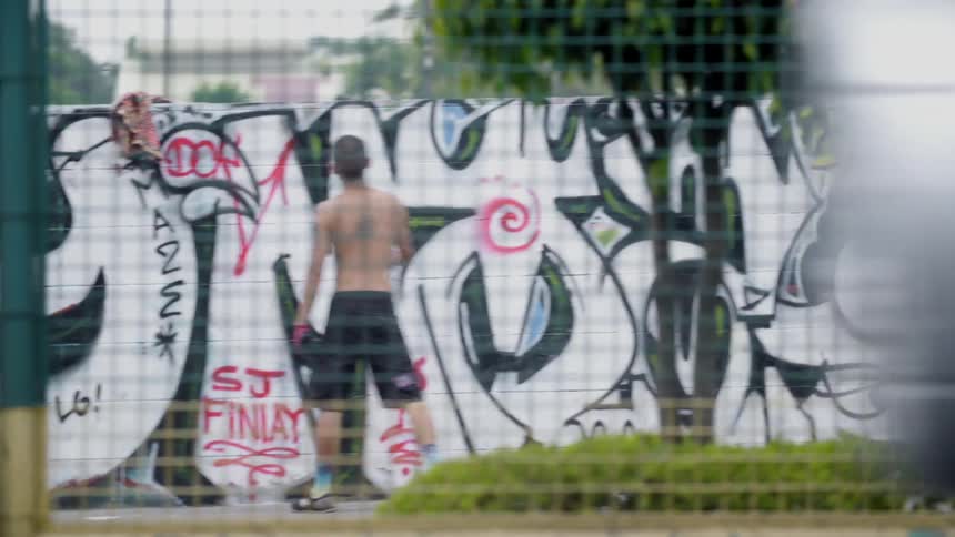 A shirtless man spray paints a wall