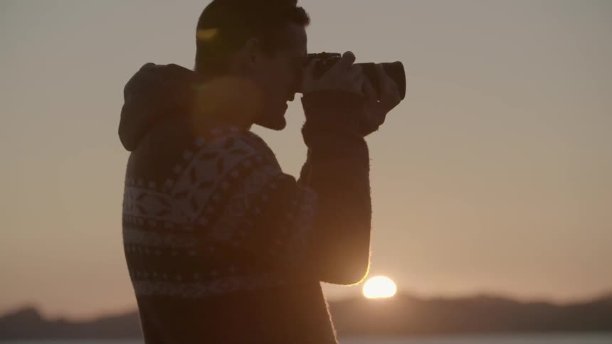 Man holding camera up to his face at sunset