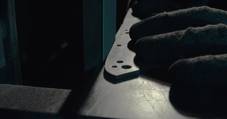 Worker wearing gloves grinds a knife on a power grinder in a workshop