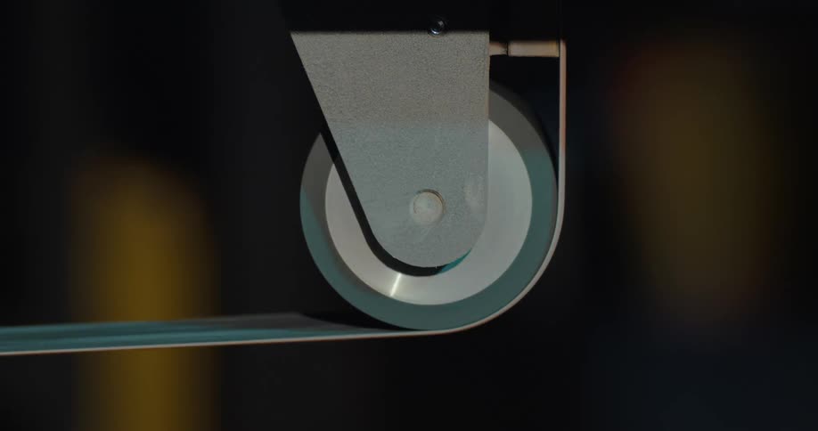 A gray metal pulley or belt is operating while a person walks past behind it