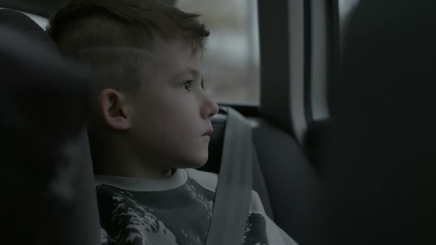 A young boy sits as a passenger in a car and looks out the window