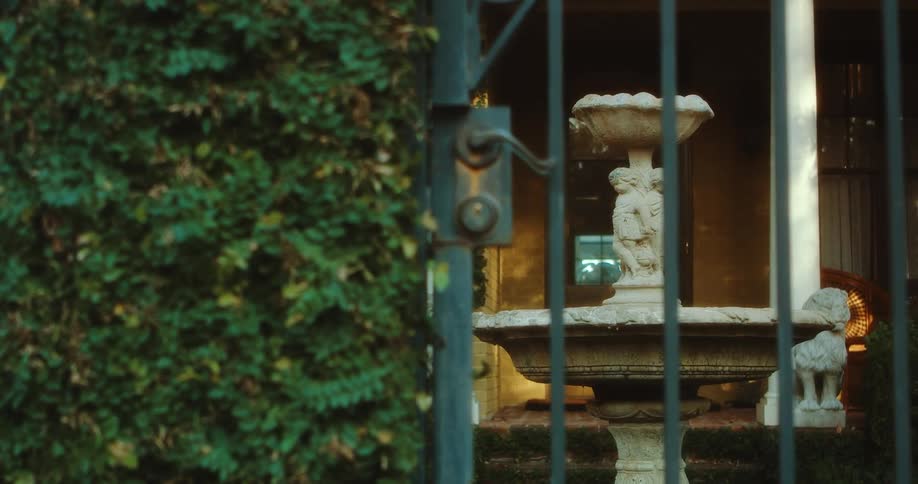 A stone bird bath sits between two columns with lion statues outside a house
