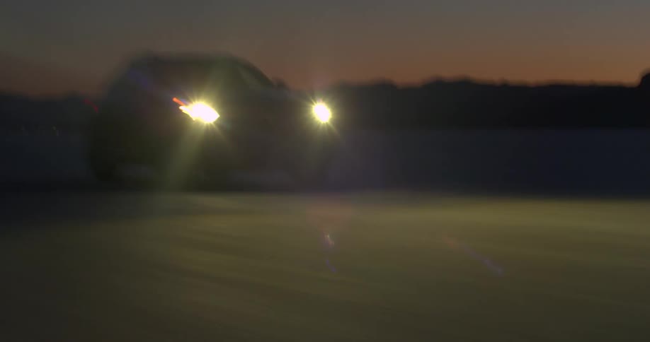 A sport utility vehicle speeds along an open dirt road at night with its headlights on