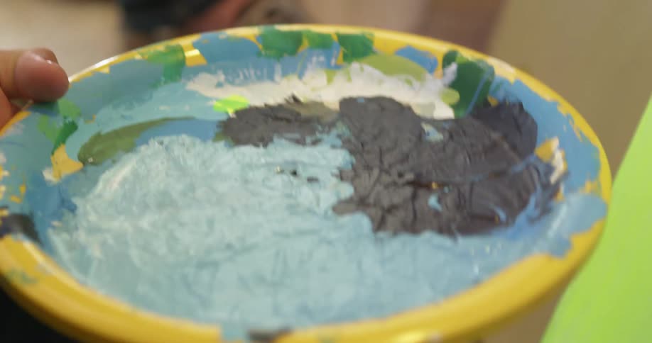 A painter uses a paper plate as a palette while painting on a canvas
