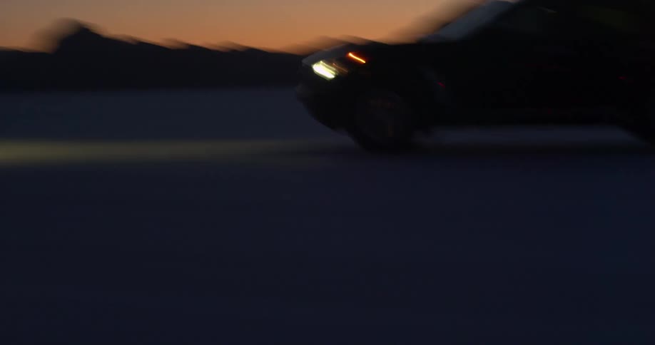A vehicle driving in the desert with a mountain range the sky and clouds in the background